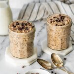 Two jars of cookie dough overnight oats with chocolate chips and spoons nearby.