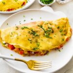 Cooked cottage cheese omelette on a white plate topped with chives served with a fork.