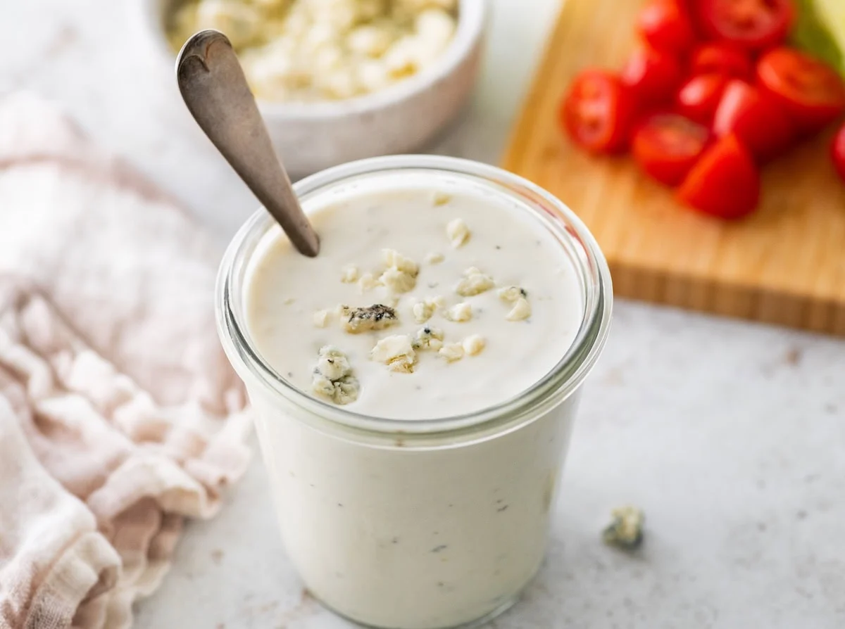 A glass jar of Greek yogurt blue cheese dressing with crumbled blue cheese pieces on top.