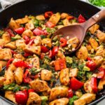 Close-up of kung pao chicken with bell peppers and broccoli being stirred.