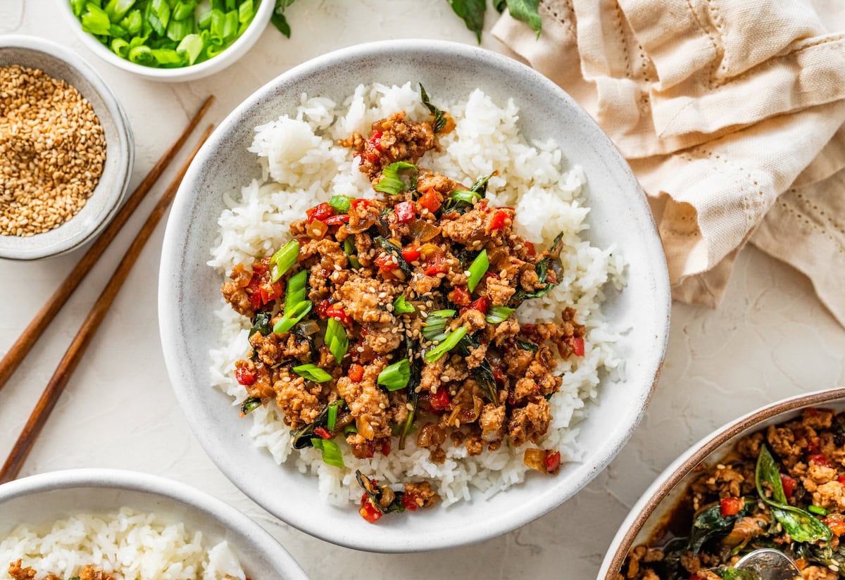 Thai basil chicken spooned over rice with fresh basil and green onions sprinkled on top.